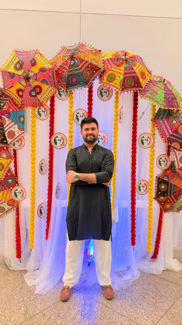 Malav Naik in a black kurta in front of colourful umbrellas and marigold garlands – Why '2 Hours of Maintenance' Becomes 3 Days: The Engineering Behind Failed Deployments and Rollbacks